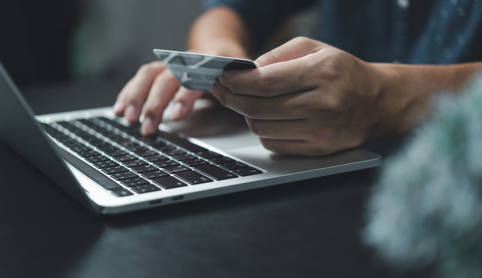Person holding a credit card while shopping for Grease Monkey weed online using a laptop
