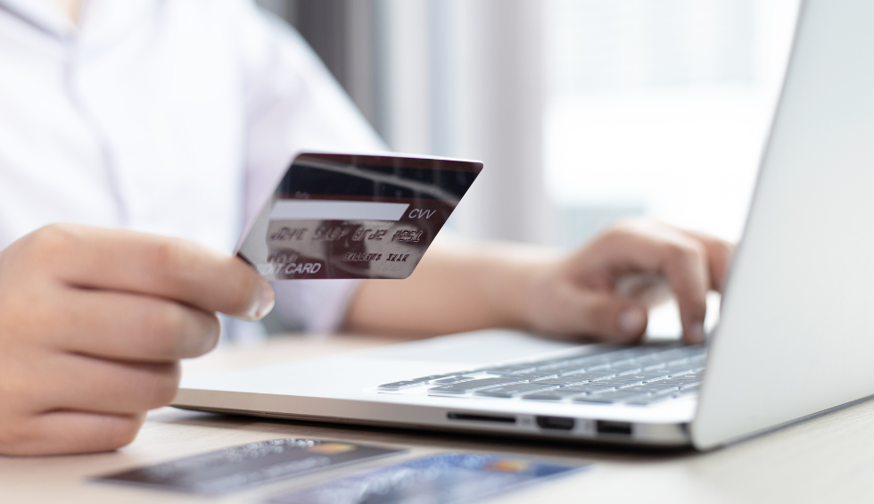 A person holding a credit card while shopping online with a laptop, representing the purchase of Sativa cannabis strains in Canada