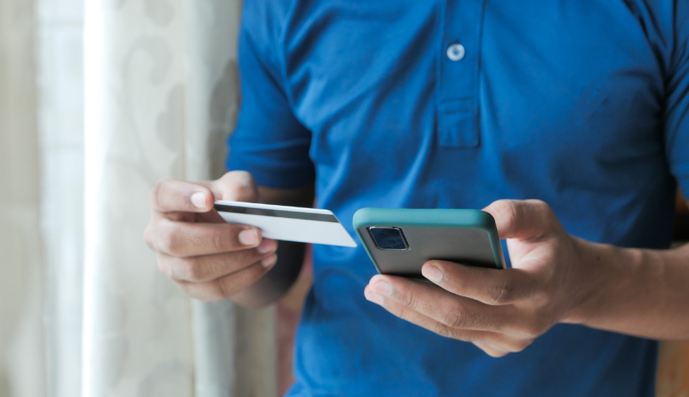 Person in a blue shirt using a smartphone and credit card to buy the Fruity Pebbles strain online