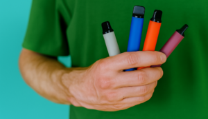 Person holding four colorful disposable weed pens, illustrating the convenience and simplicity of disposable vape options