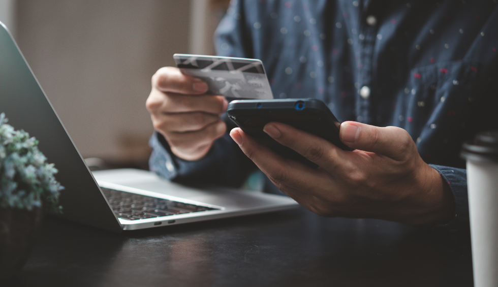 Person holding credit card and smartphone near laptop, symbolizing quick canna online purchase from a nearby dispensary