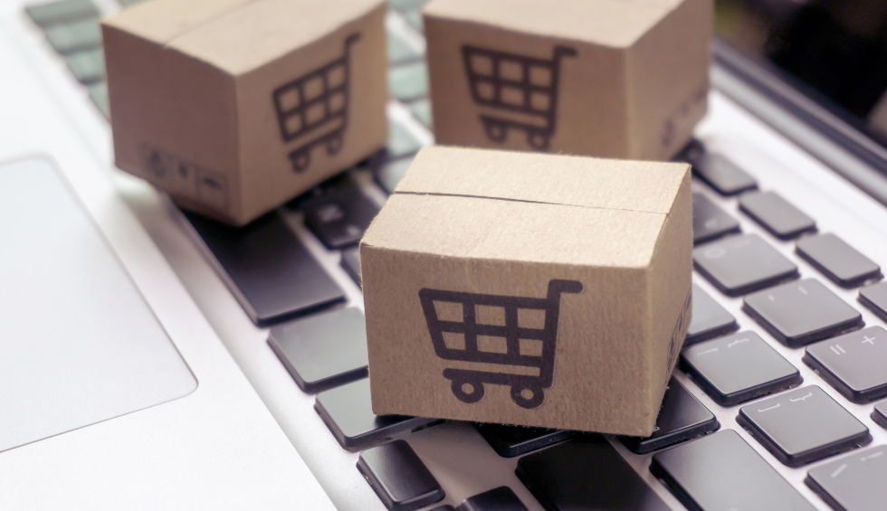Small cardboard boxes with shopping cart icons on a laptop keyboard, representing weed online shopping convenience