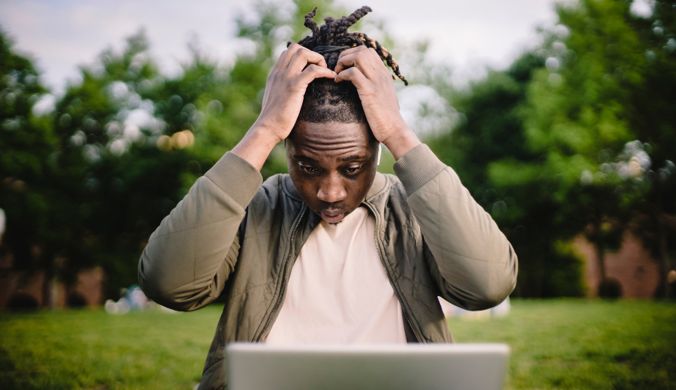 Man sitting outdoors looking frustrated while using a laptop, symbolizing common mistakes to avoid when buying weed online in Canada