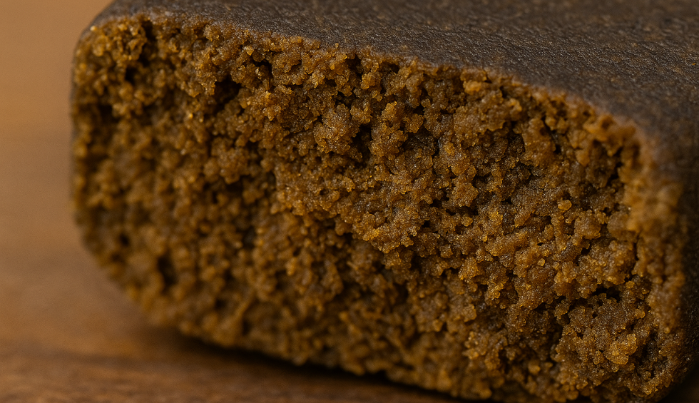 Close-up of dense brown cannabis hash showing crumbly interior texture on wooden surface